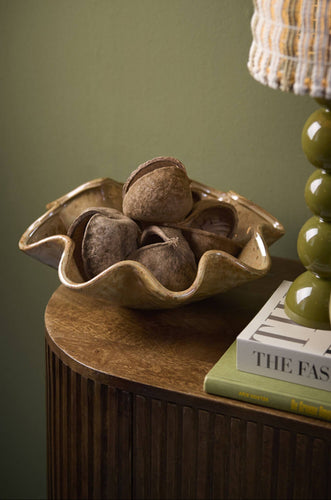 Schaal Godeni gevuld met gedroogde decoratieve zaadpeulen op een houten dressoir met tafellamp en boeken